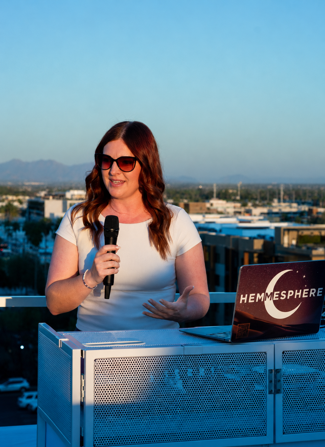 Female Arizona wedding and event DJ speaking at a rooftop venue overlooking the Scottsdale skyline. DJ Hemmesphere brings over 18 years of experience, blending EDM roots with crowd-focused music programming for weddings, corporate events, and private celebrations.